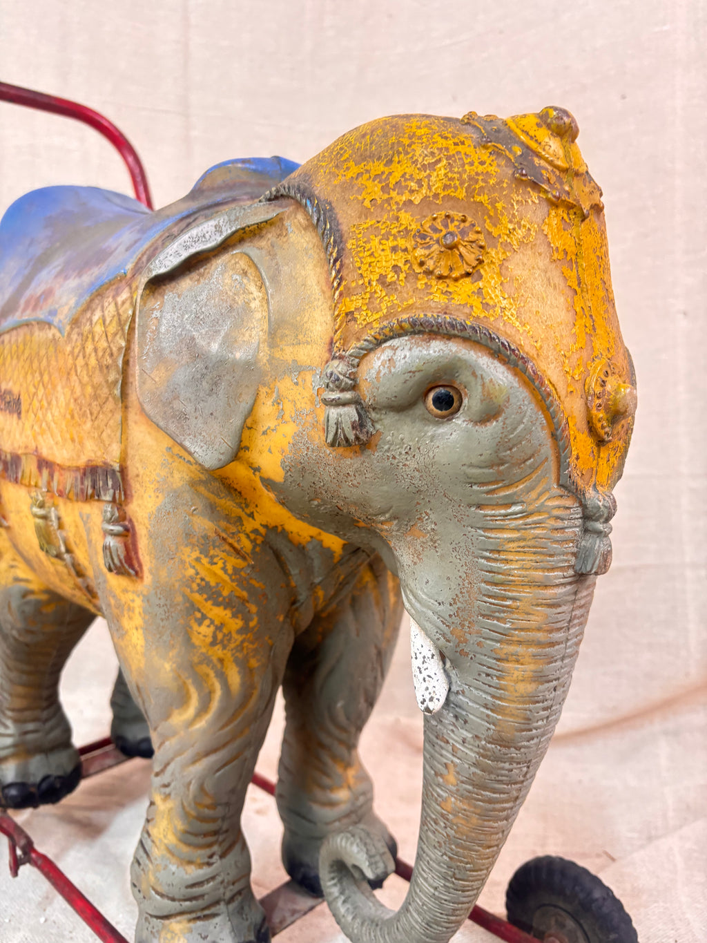 Vintage 1950s Tri-ang push-along elephant toy with hard plastic body, blue saddle, and red metal chassis with rubber wheels