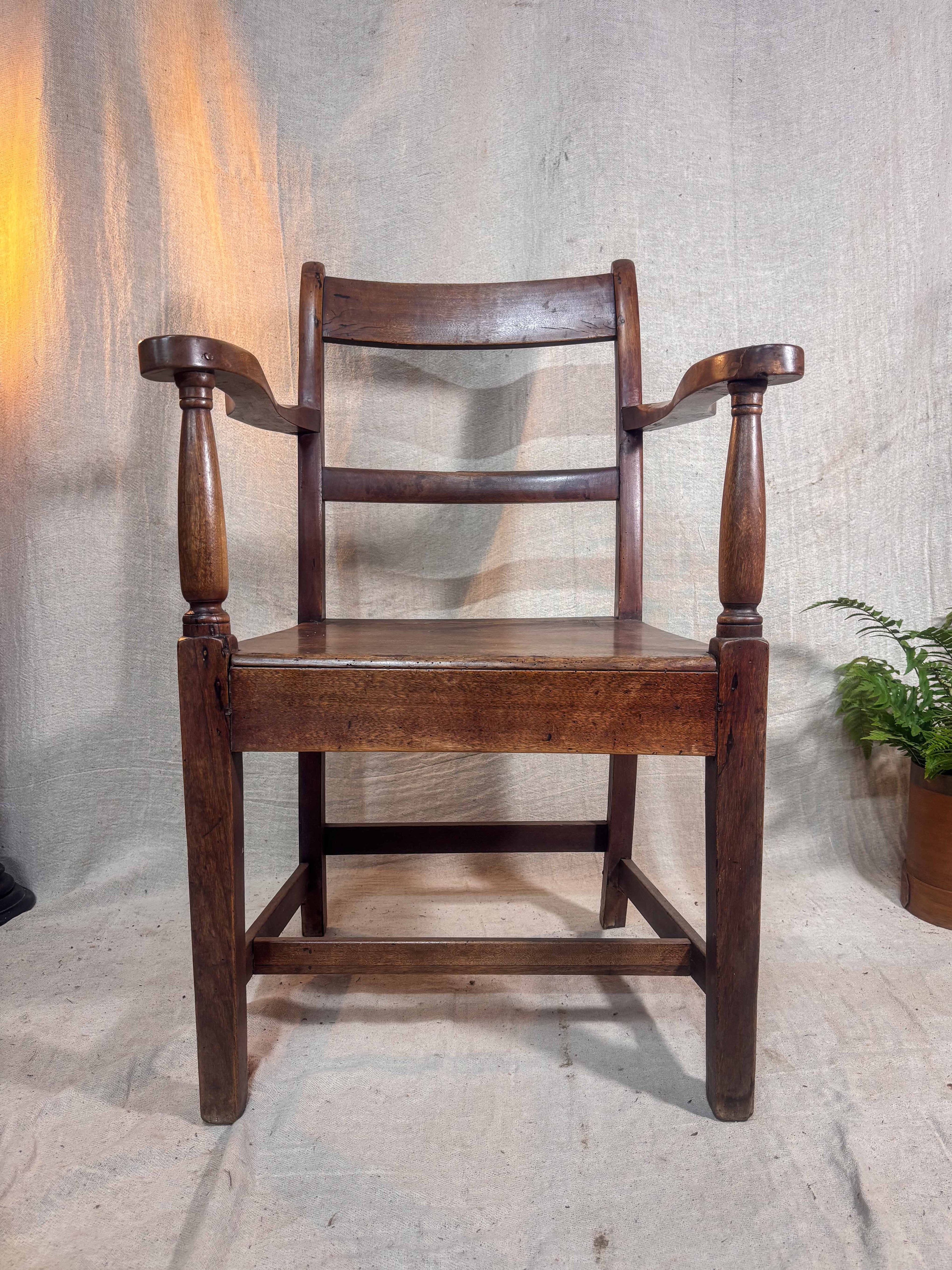 Wooden chair with armrests against a textured wall.