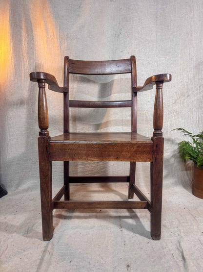 Wooden chair with armrests against a textured wall.