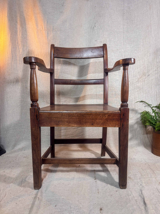 Wooden chair with armrests against a textured wall.