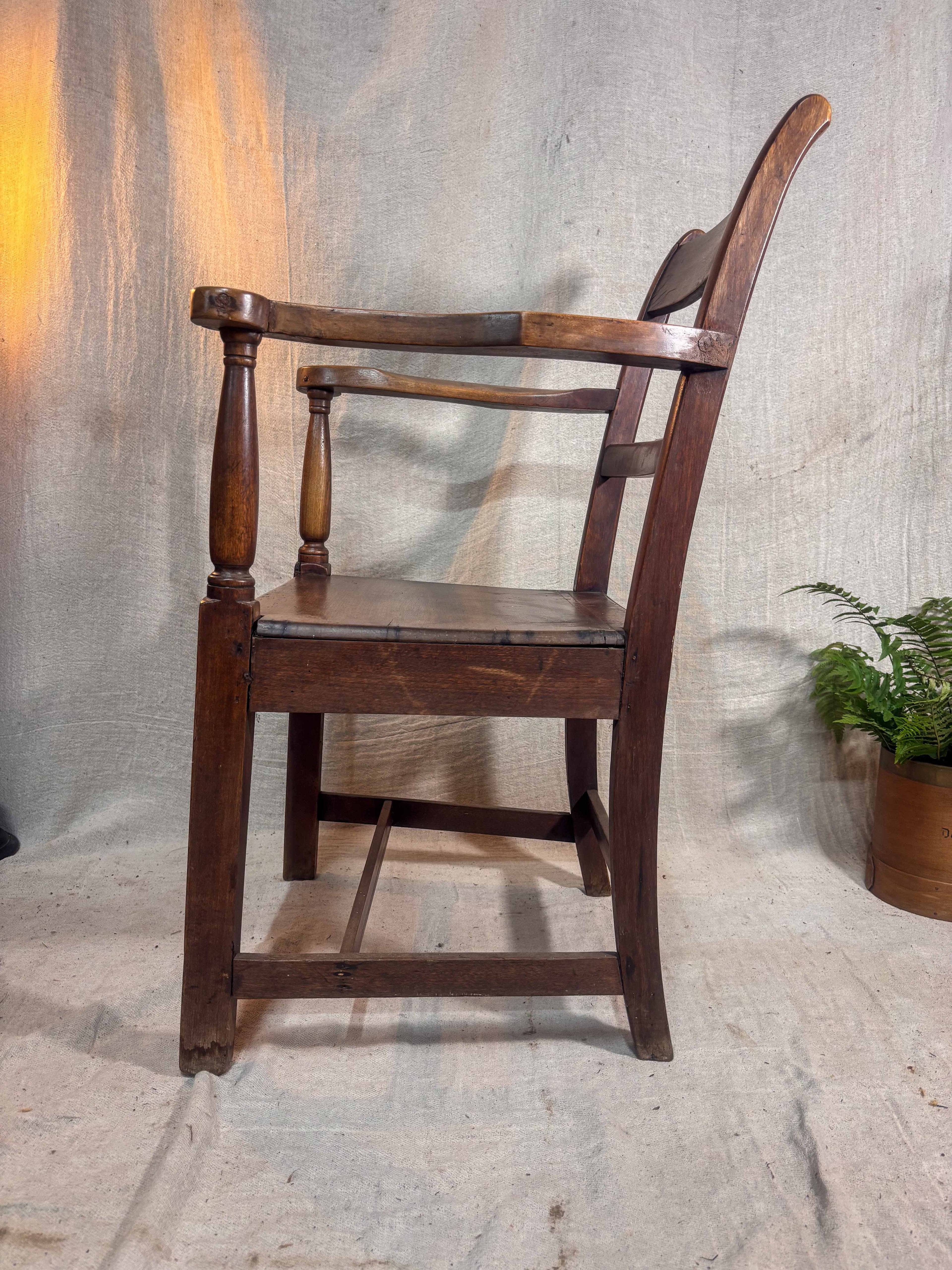 Wooden chair with a plant in the background on a textured floor.