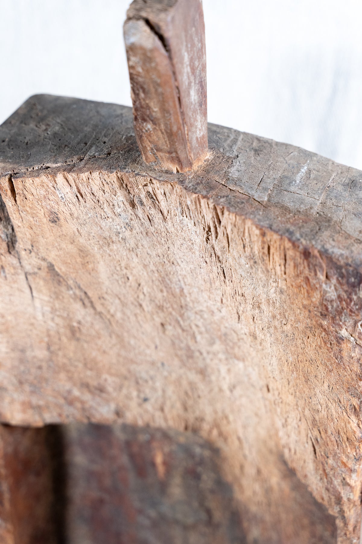 Close-up detail of a rustic, weathered wooden object showing the textured grain and a small protruding wooden piece against a light background.