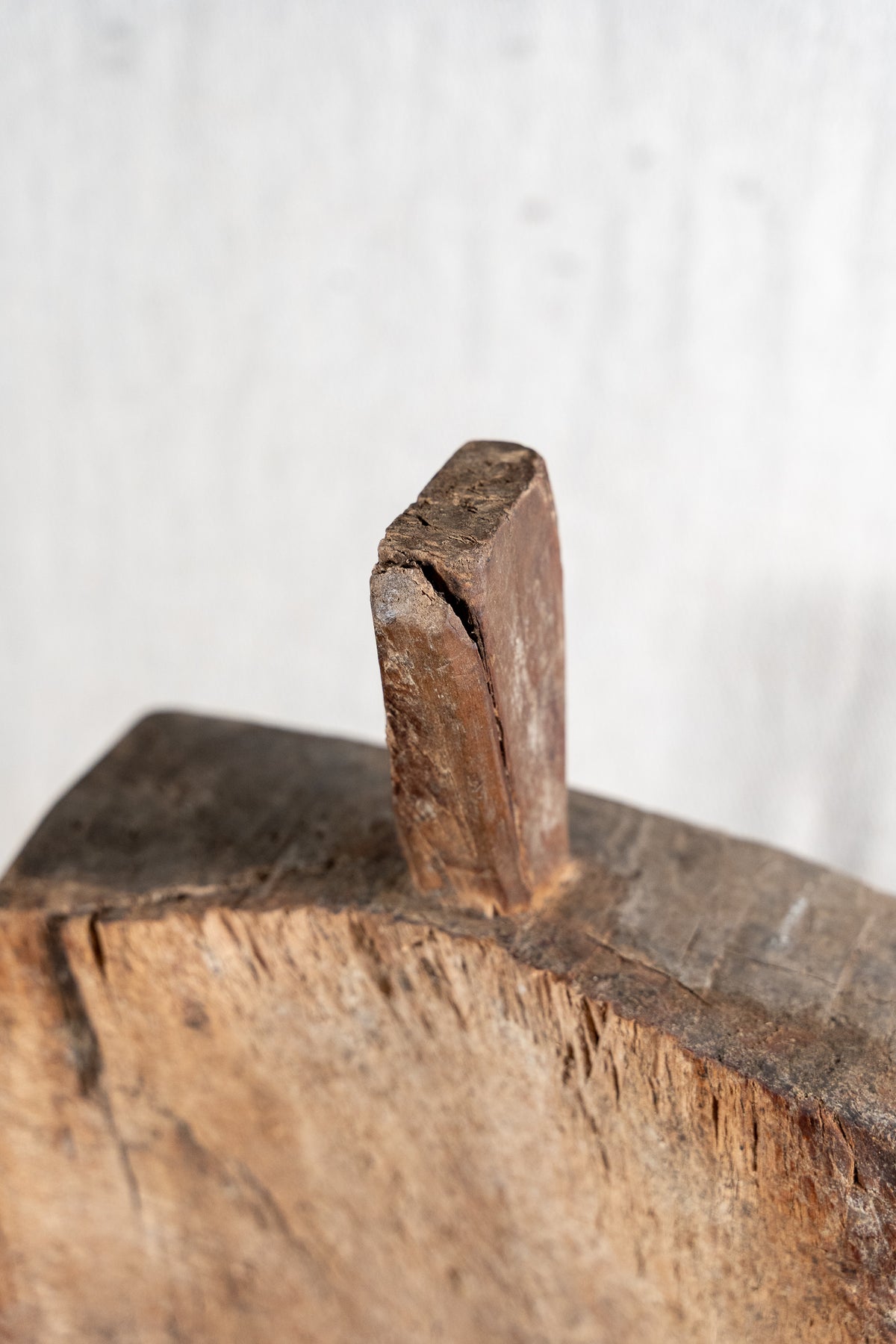A close-up of a rustic, weathered wooden peg or knob protruding from a rough, natural wood block against a light, textured background.