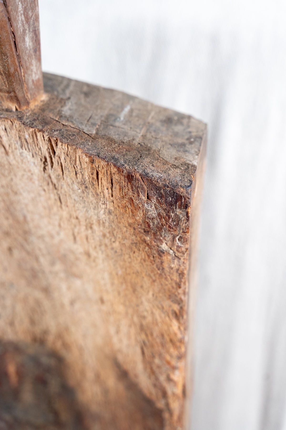 Close-up detail of a rustic wooden furniture corner, showing the rough natural wood grain and texture against a blurred light gray background.
