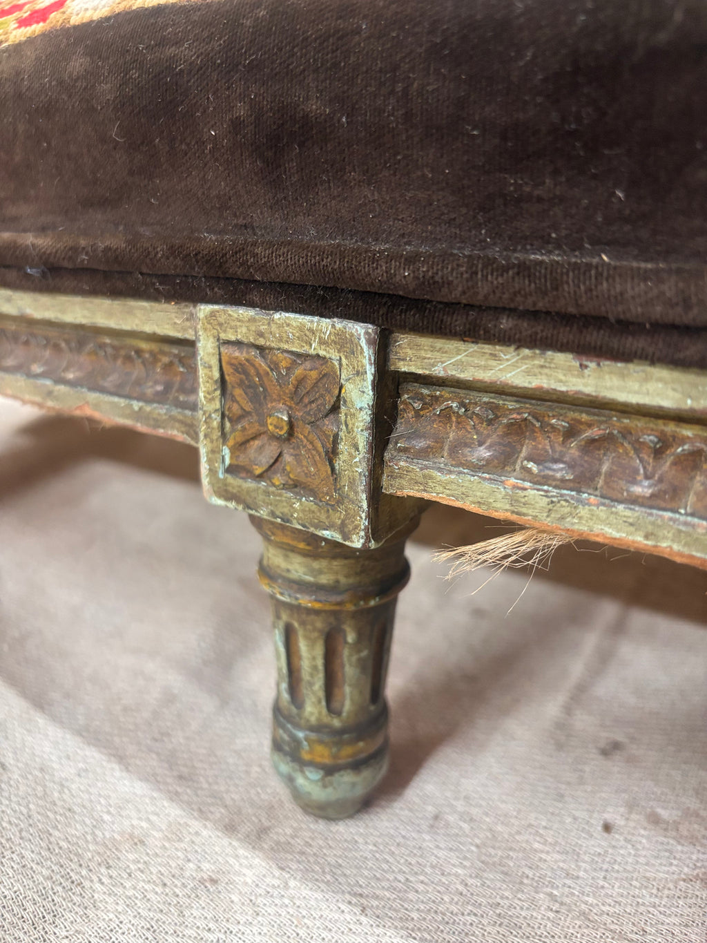 Close-up of a decorative wooden leg with intricate carvings on a brown upholstered surface.