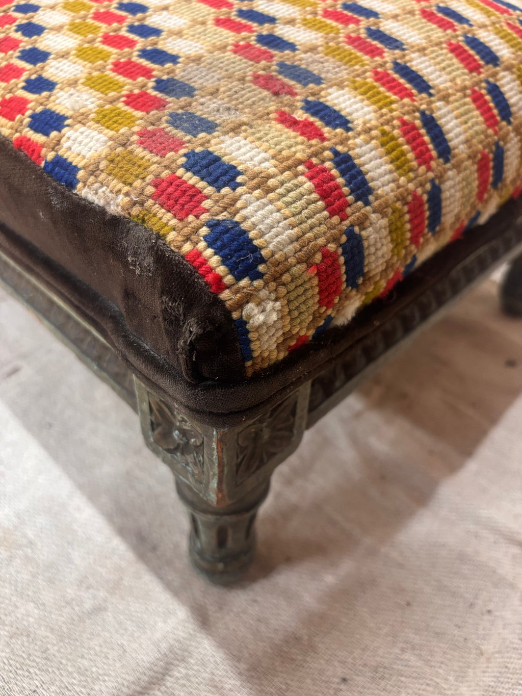 Close-up of a patterned stool with decorative legs on a light-colored floor.
