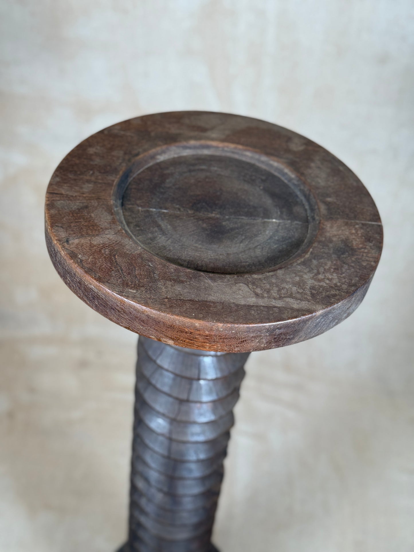 A close-up of a rustic wooden top with a circular center recess, mounted on a dark metal threaded stem, set against a neutral beige background.