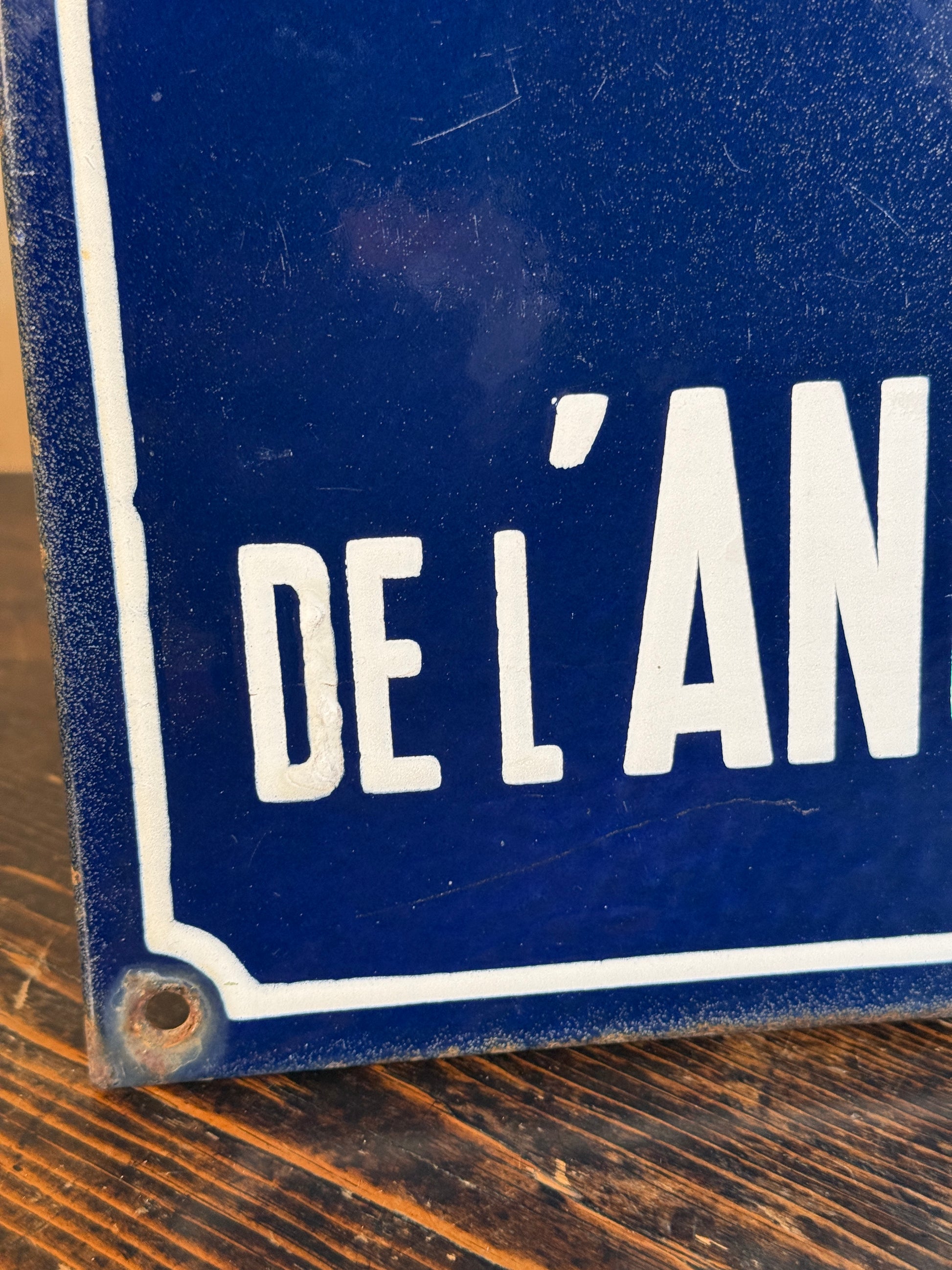 A close-up of a blue enamel sign with white lettering reading 'DE L'AN.
