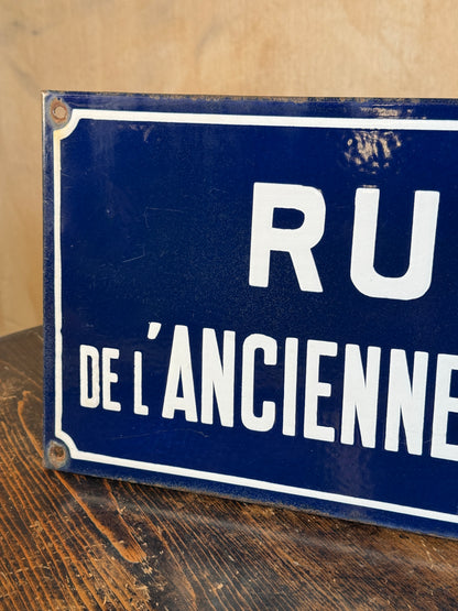 A close-up of a vintage blue enamel street sign with white lettering reading 'RU DE L'ANCIENTE' on a wooden surface.