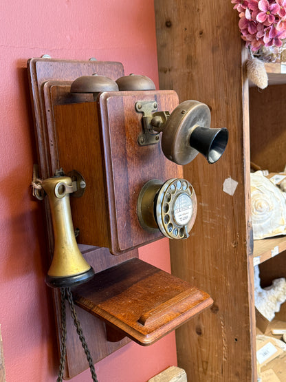 Vintage wooden telephone with brass components on a pink surface