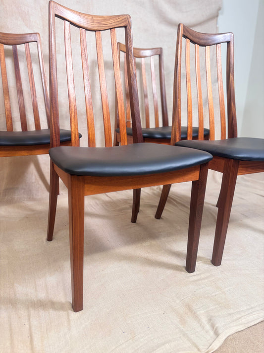 Four mid-century modern wooden dining chairs with spindle backs and black upholstered seats, arranged on a beige fabric floor cover.
