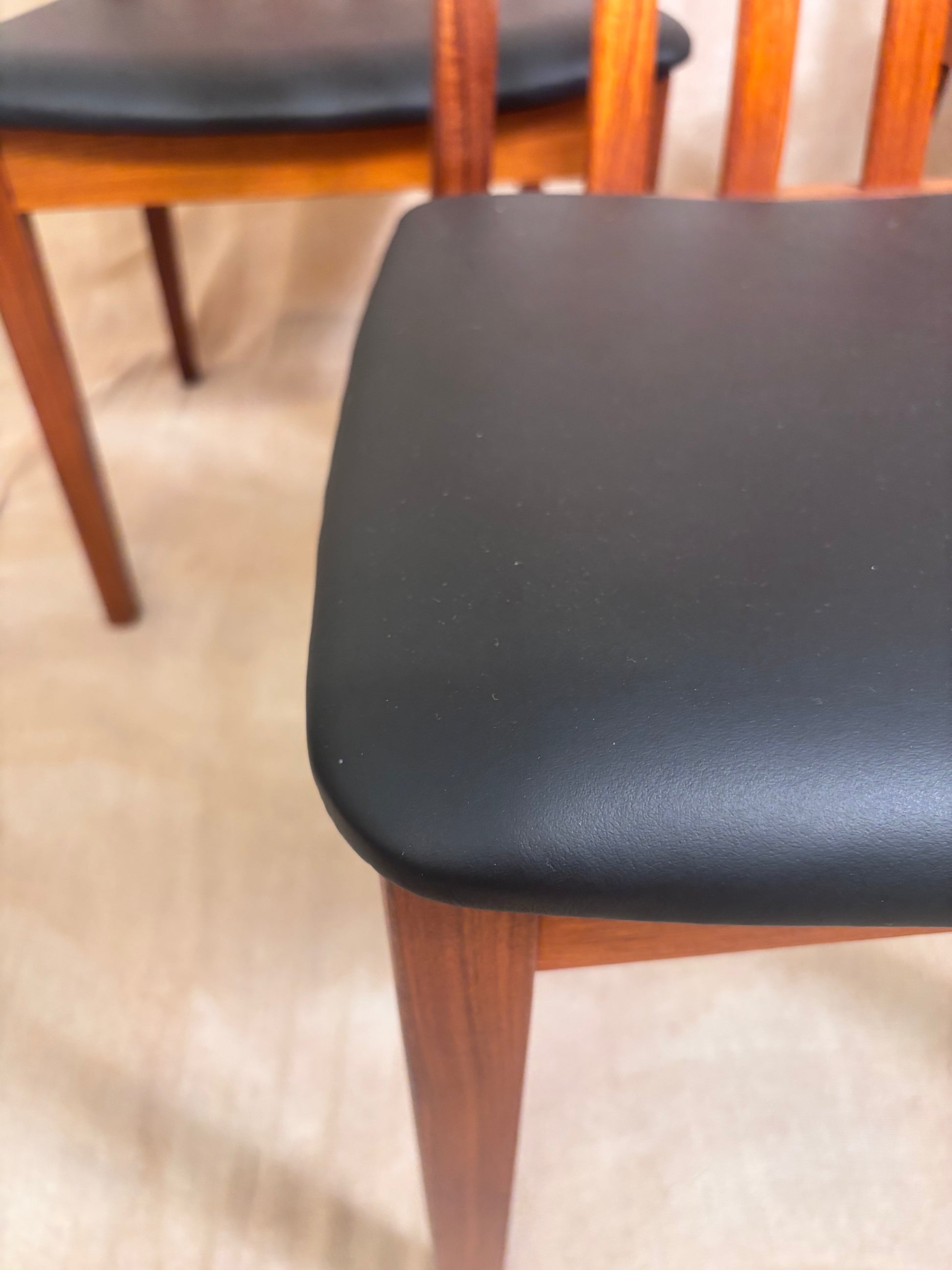 Close-up of a wooden dining chair with a black upholstered seat cushion and reddish-brown wood legs, shown indoors on a light floor.