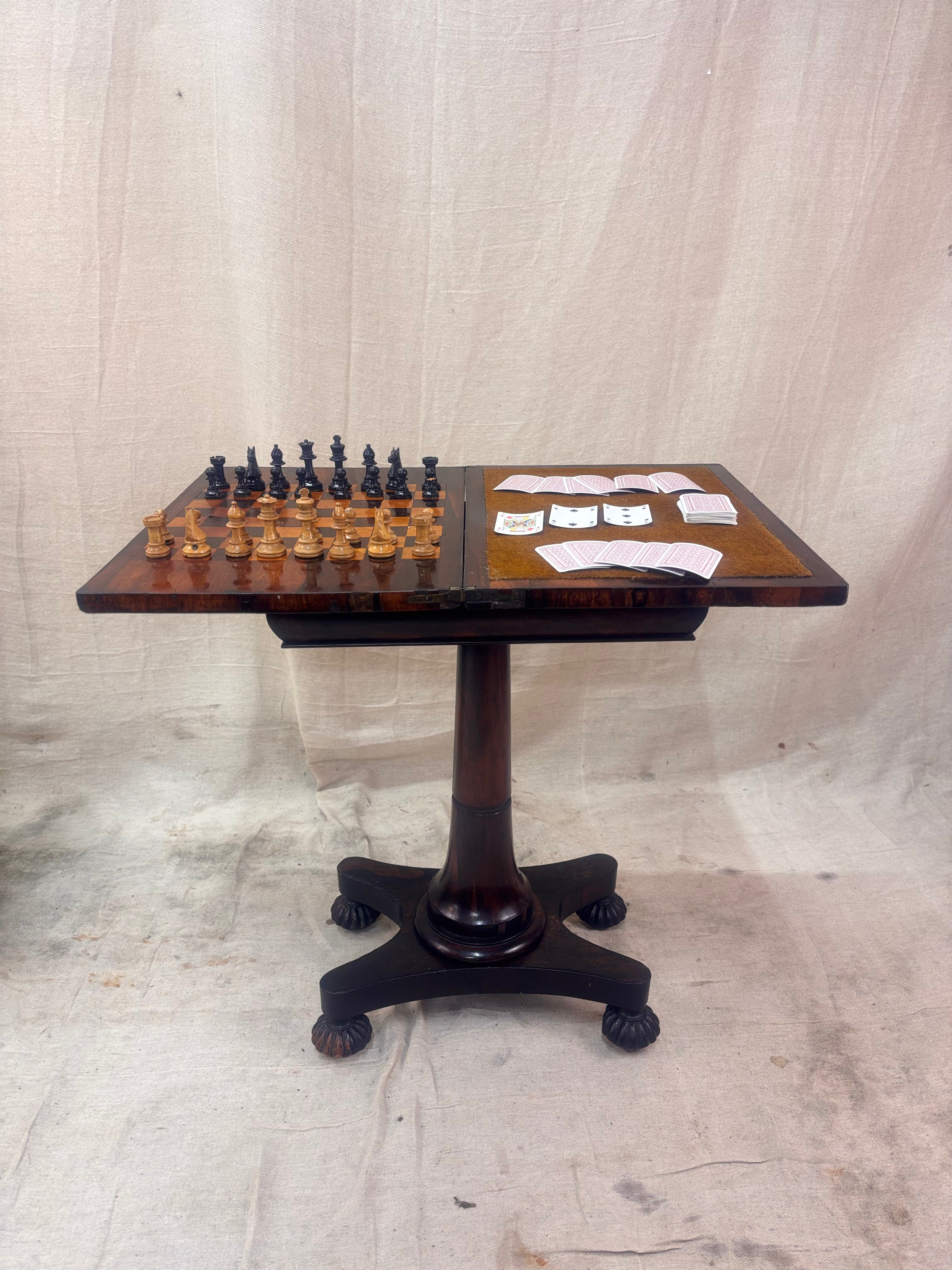 Antique rosewood fold-over games table with inlaid chessboard, baize card surface, turned pedestal base, shown open with chess pieces and playing cards.