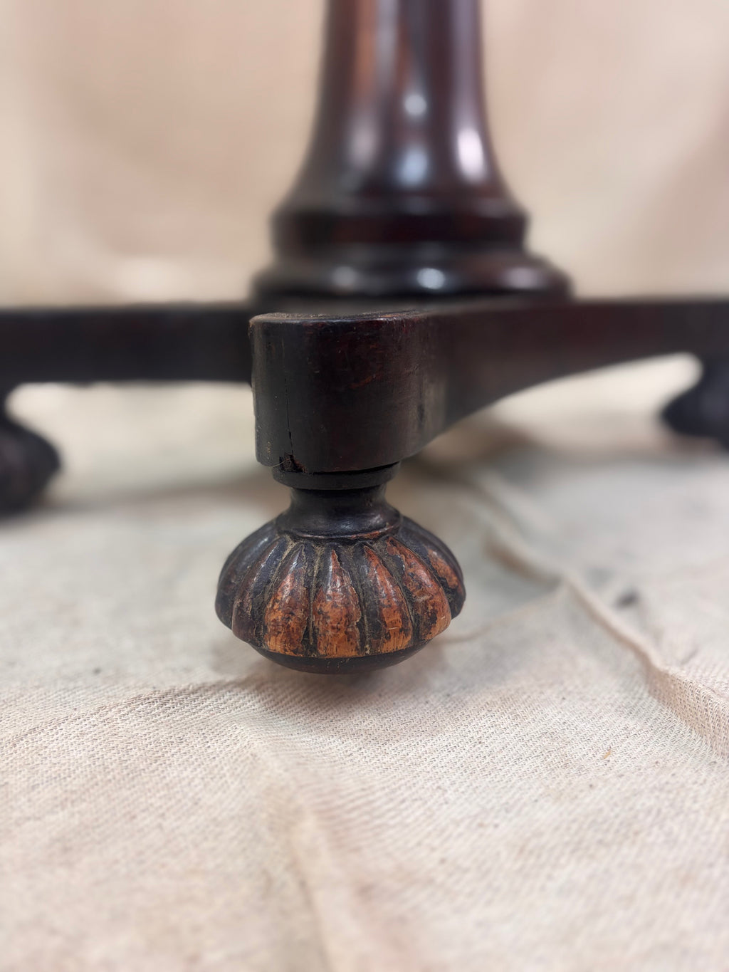 Close-up of a wooden table leg with a textured surface on a beige fabric background