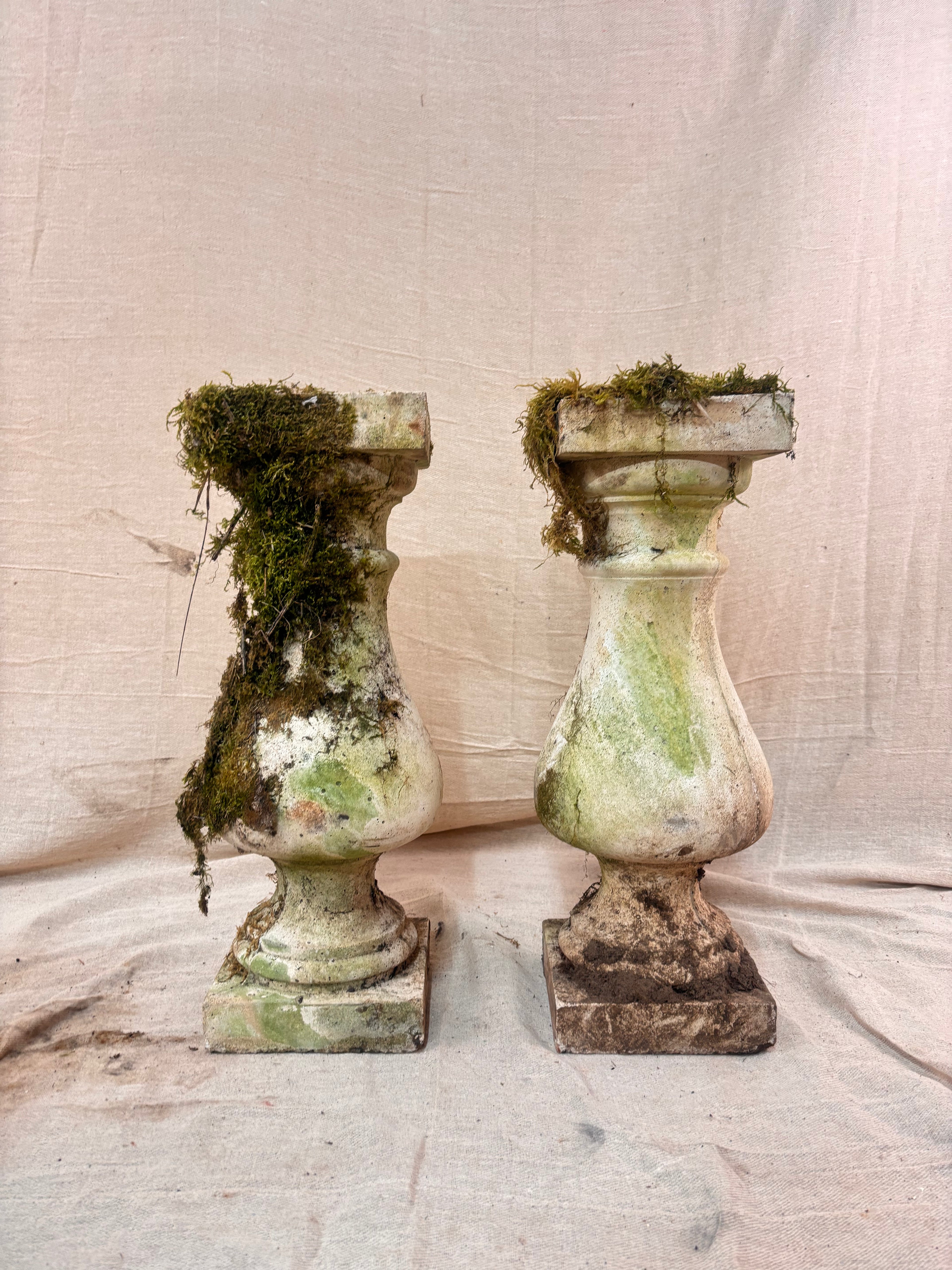 Vintage stone garden pedestals with a classic baluster shape, stepped square bases, and flat square tops, finished in weathered pale gray stone with natural moss and lichen growth.