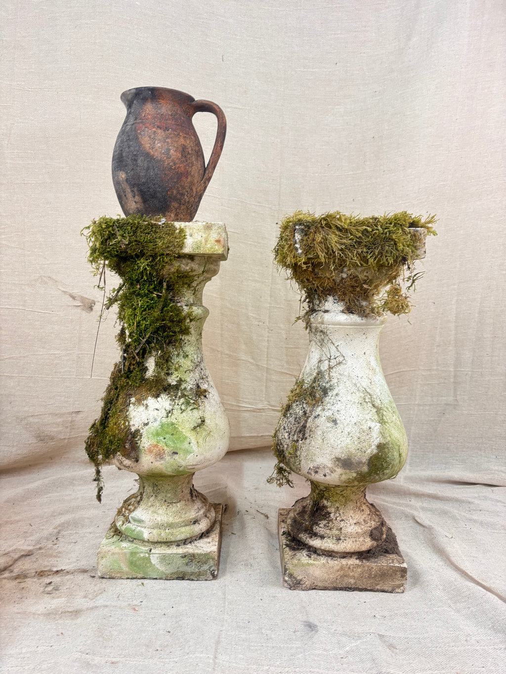 Vintage stone garden pedestals with a classic baluster shape, stepped square bases, and flat square tops, finished in weathered pale gray stone with natural moss and lichen growth.