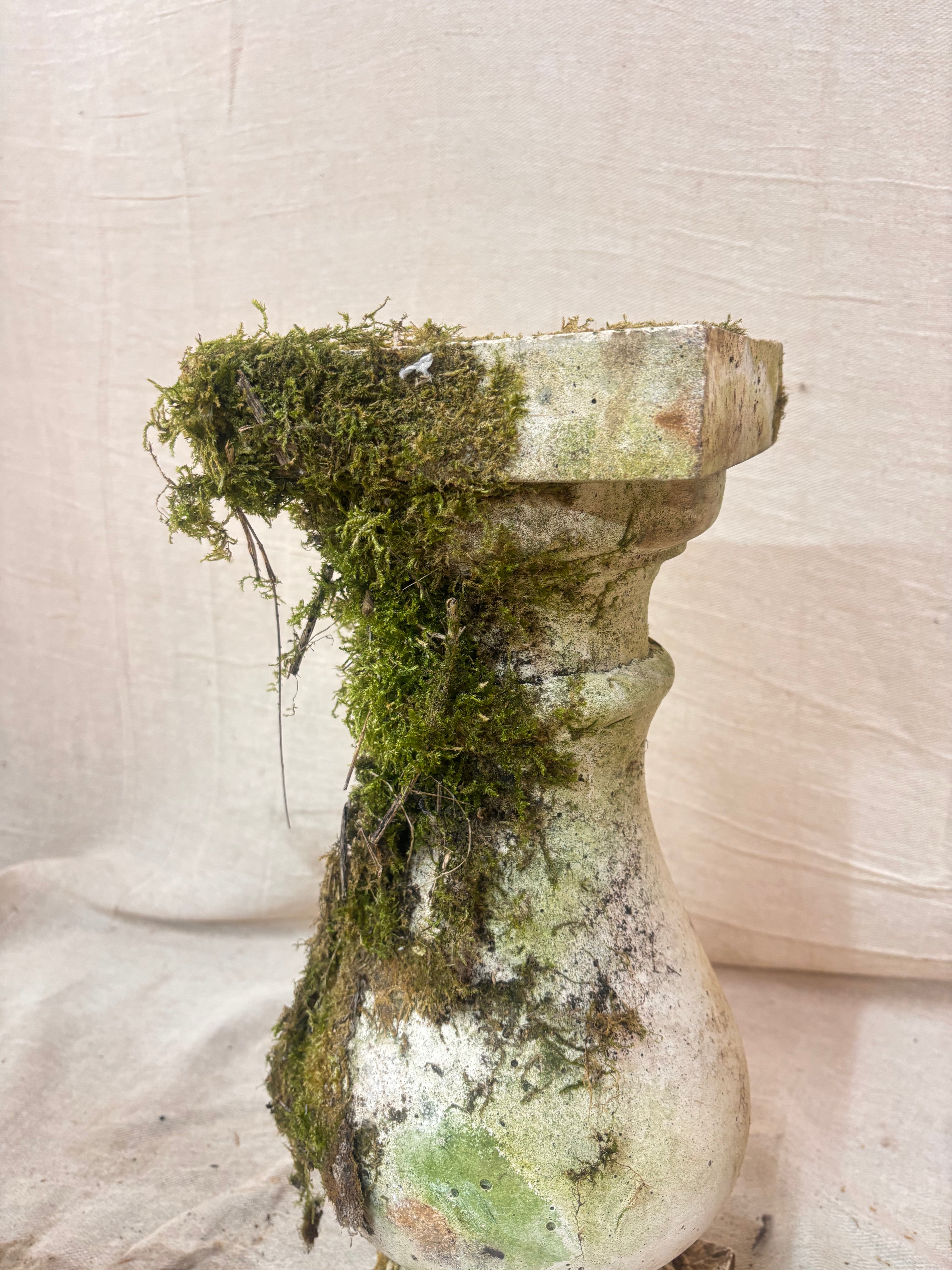 Moss-covered stone pedestal on a textured beige background