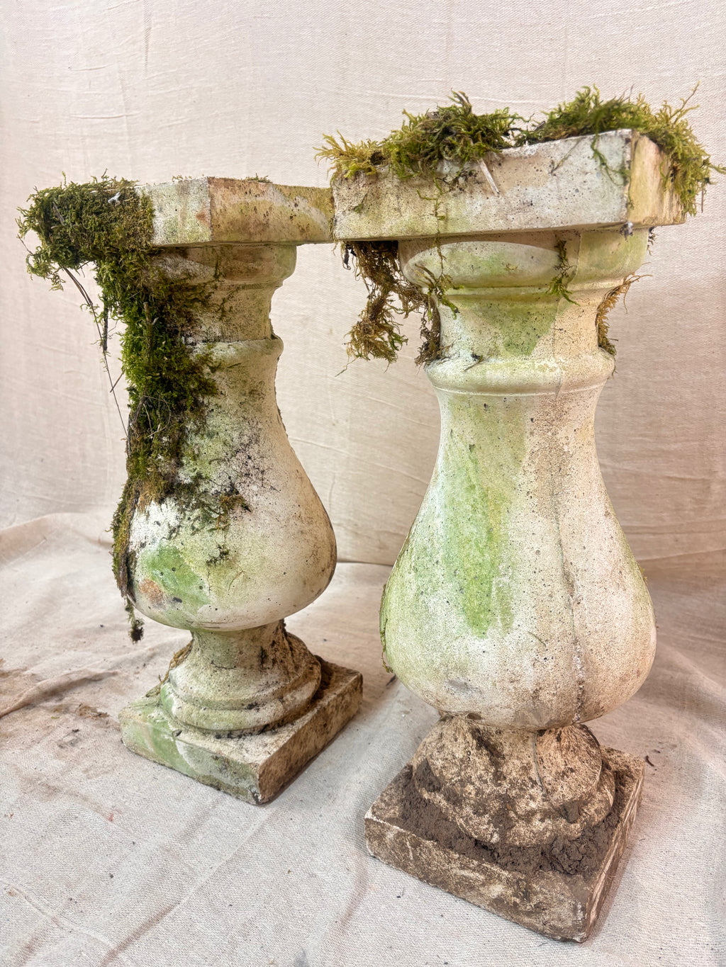 Vintage stone garden pedestals with a classic baluster shape, stepped square bases, and flat square tops, finished in weathered pale grey stone with natural moss and lichen growth.