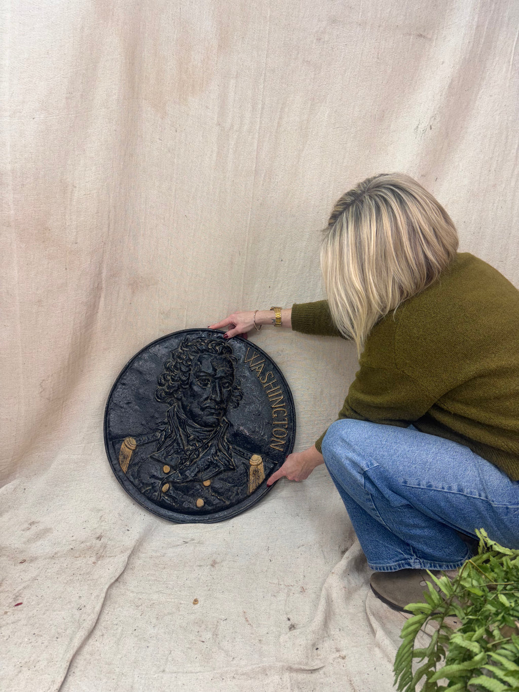 Person holding a decorative round plaque with a bust on a light fabric background
