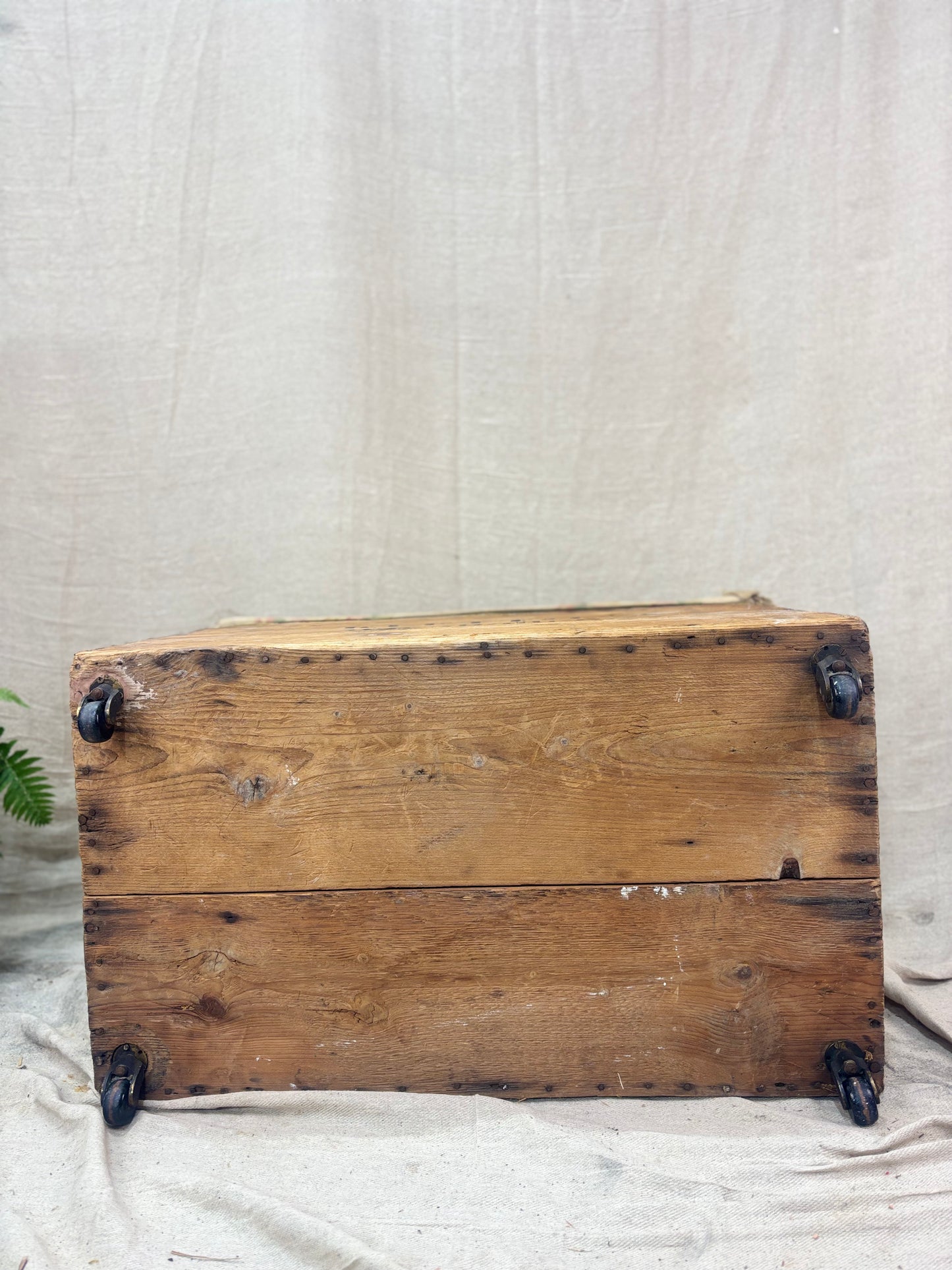 Vintage wooden crate with metal wheels on a textured beige background