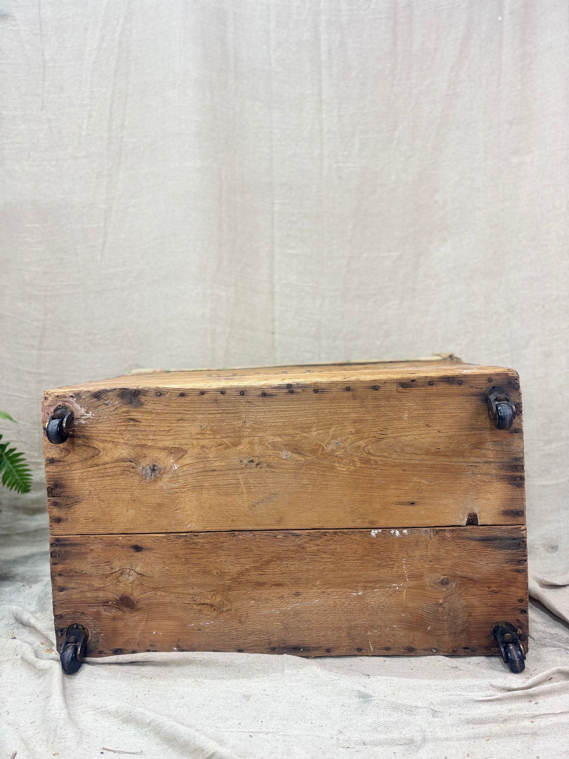 Vintage wooden crate with metal wheels on a textured beige background