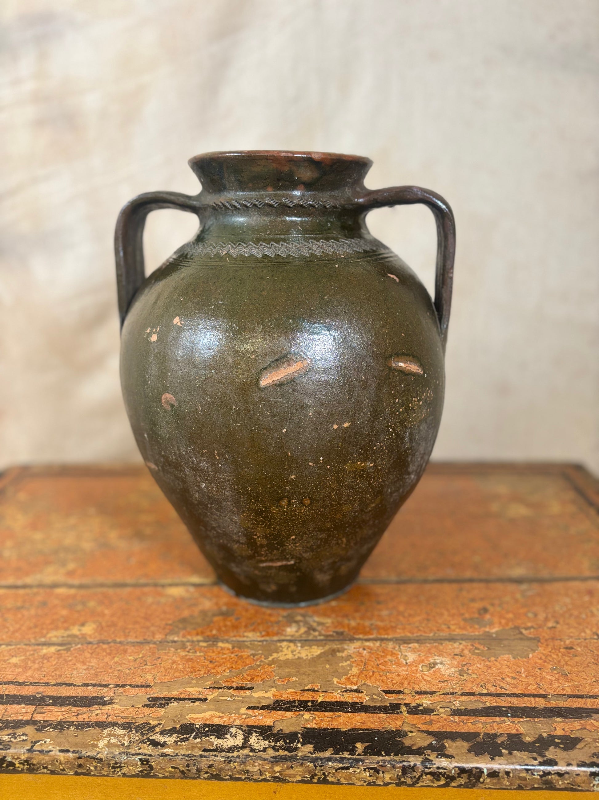 Vintage green ceramic vase with black handles on a wooden surface