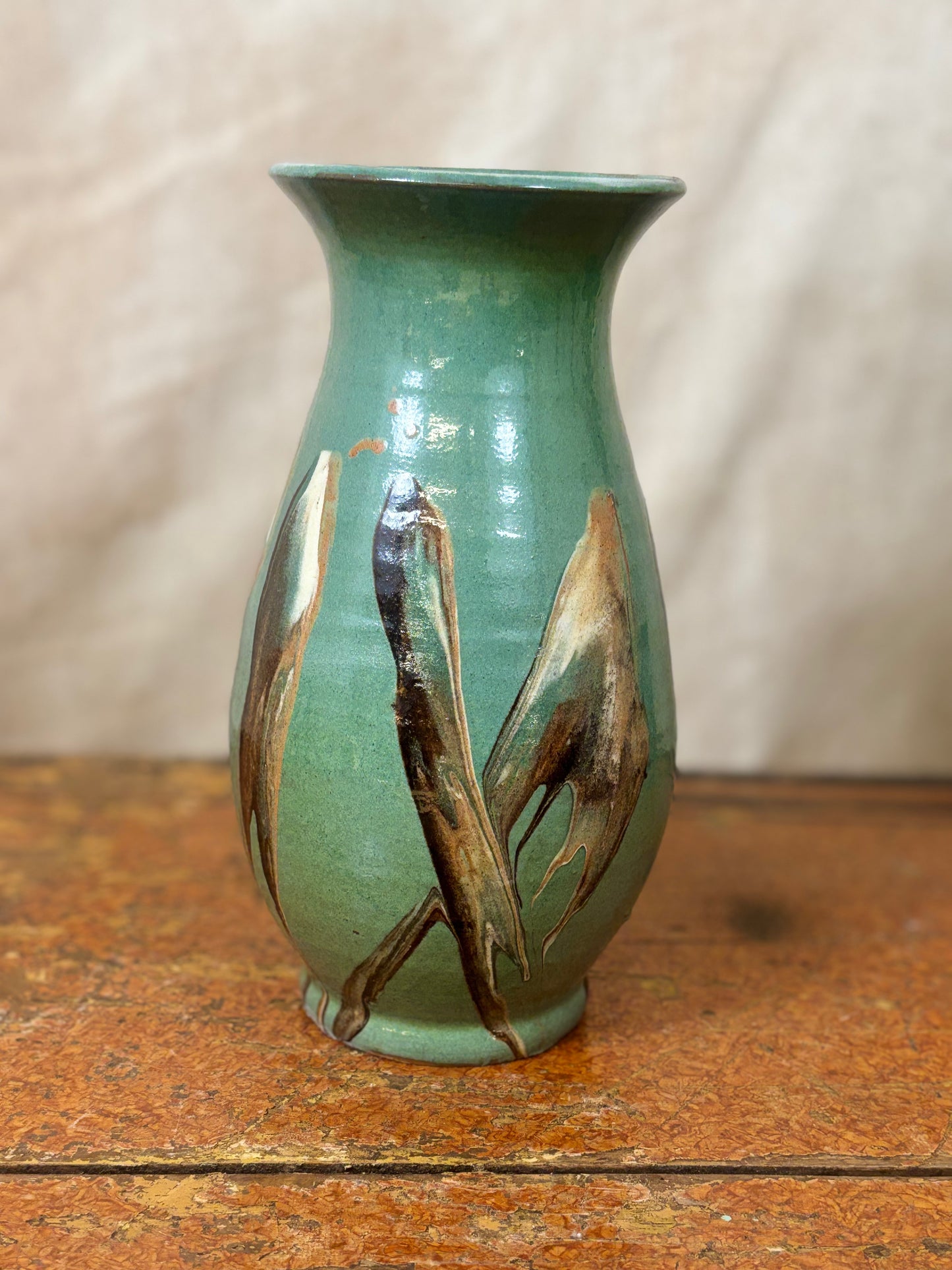 Green ceramic vase with abstract brown designs on a wooden surface