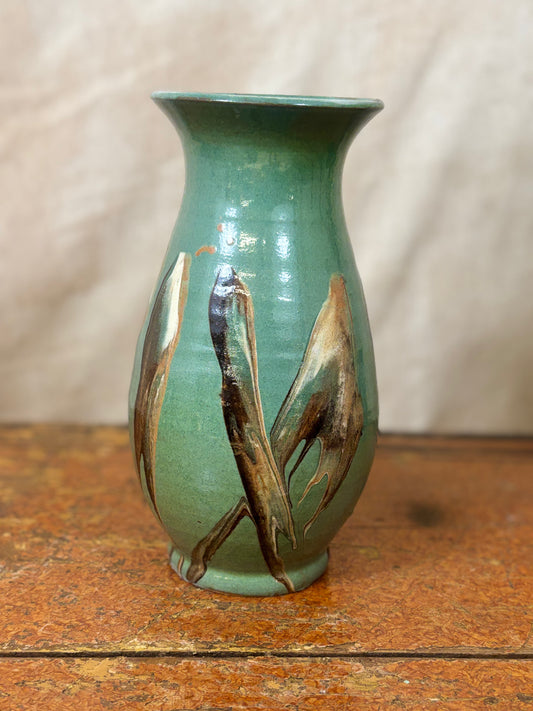 Green ceramic vase with abstract brown designs on a wooden surface