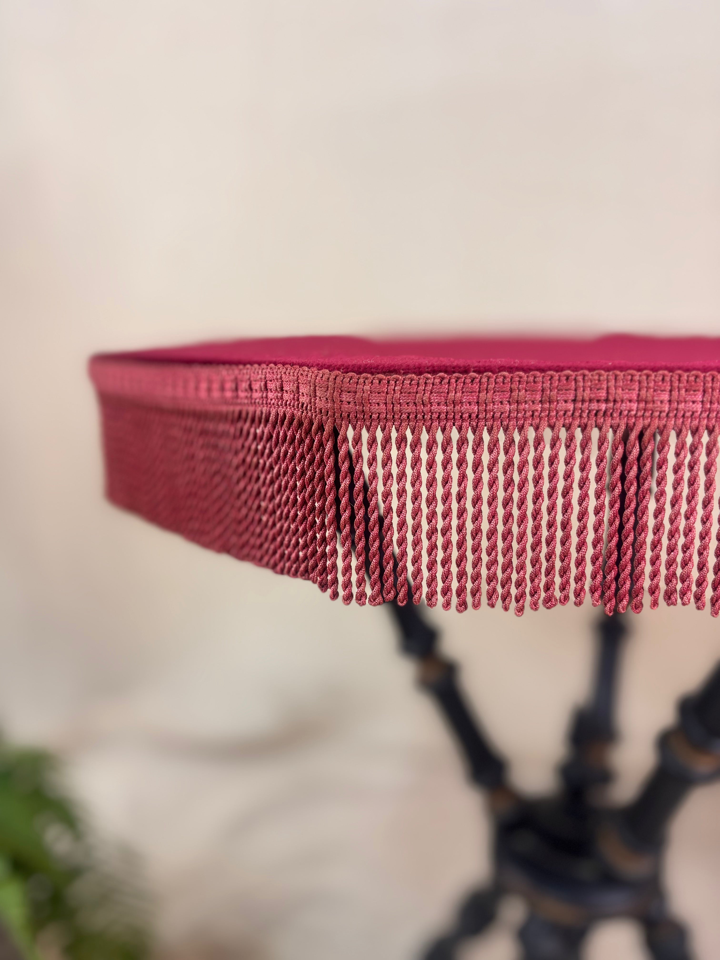 Close up of the fringing of Antique Victorian ebonized bobbin-legged gypsy table with red velvet octagonal top and fringing, photographed against a cloth backdrop next to a plant