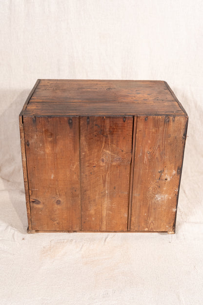 A rustic wooden storage chest or crate with three front doors, made from weathered brown wood planks, photographed against a neutral off-white fabric backdrop.