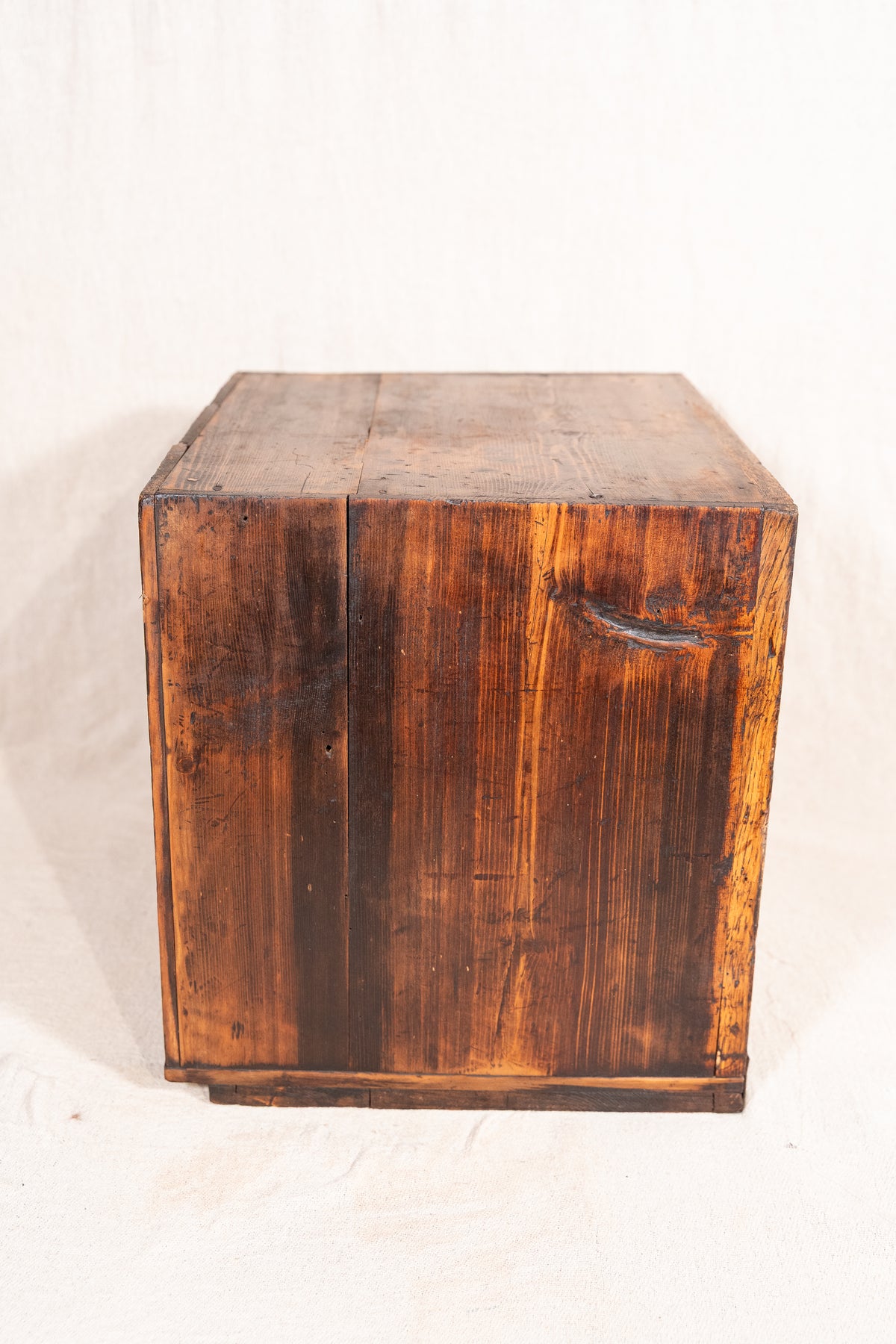 A rustic wooden storage chest or crate made of dark stained wood planks, photographed against a plain off-white fabric background.