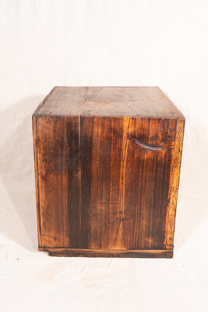 A rustic wooden storage chest or crate made of dark stained wood planks, photographed against a plain off-white fabric background.