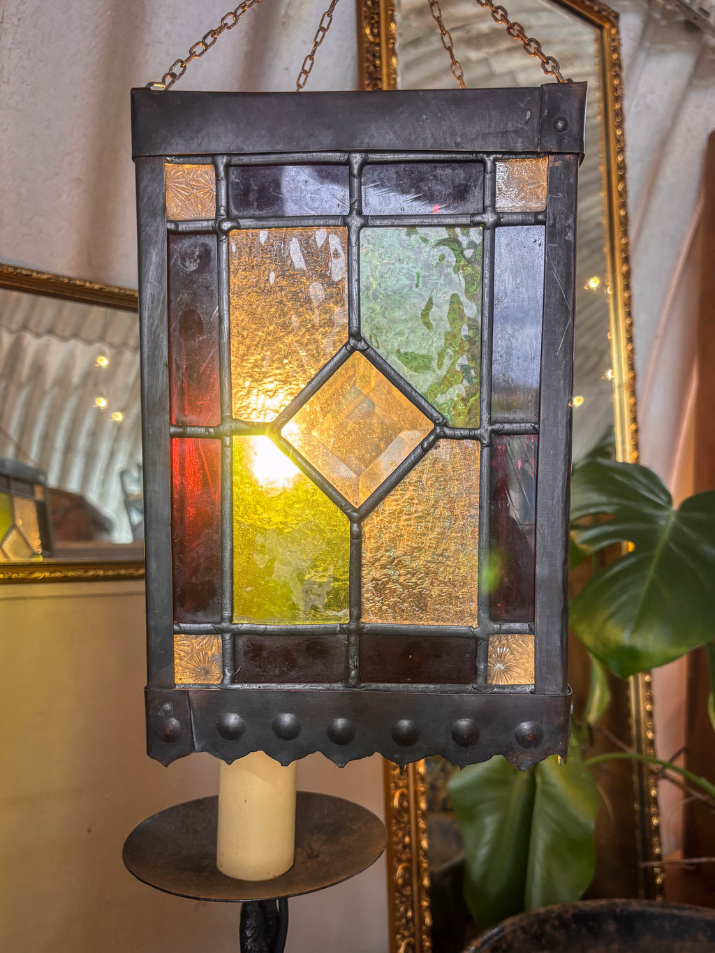 Stained glass hanging light fixture with a candle holder in a decorative setting.
