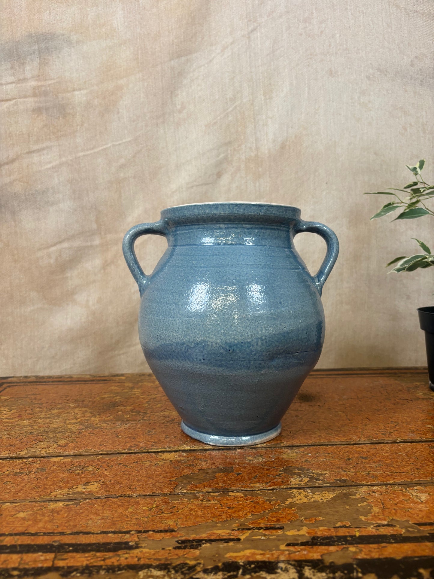 Blue ceramic vase with handles on a wooden surface against a beige wall.