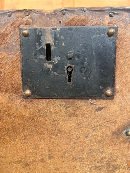 Close-up of a rustic wooden surface with a dark metal lock plate secured by four brass-colored rivets.