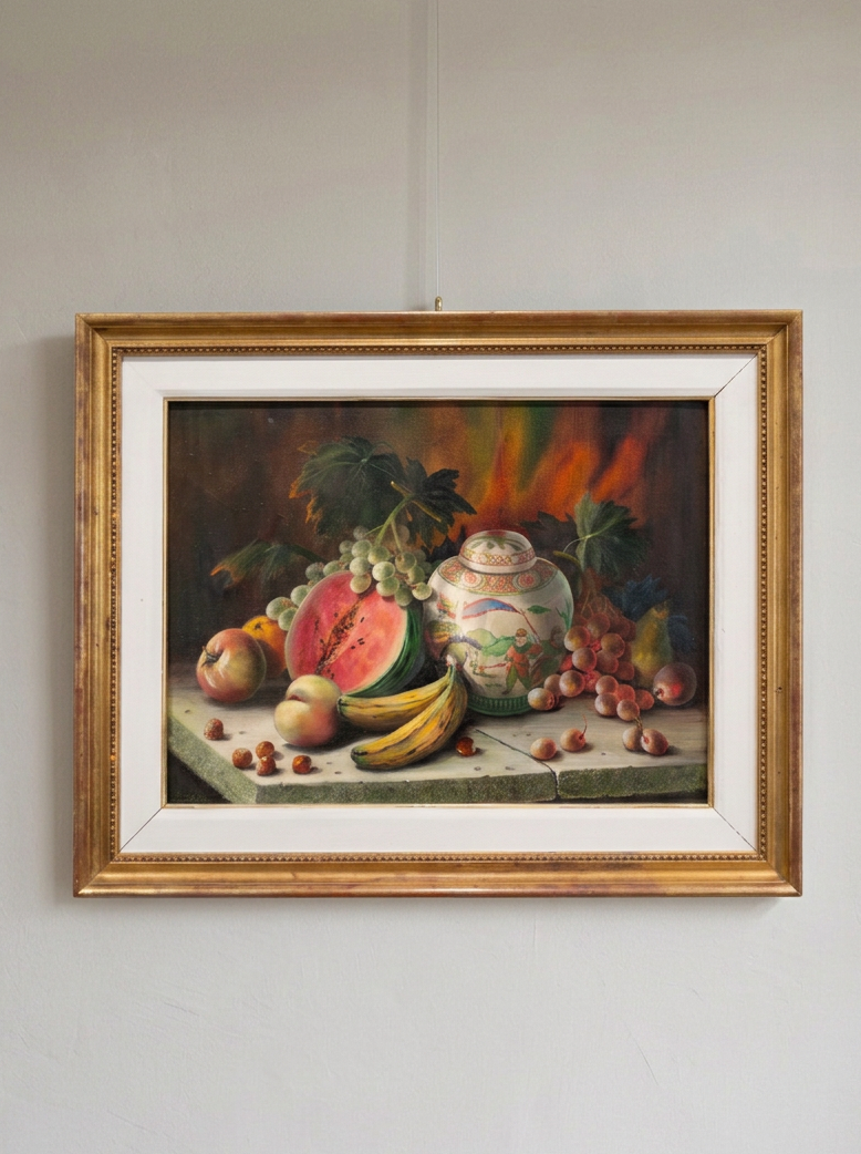 A framed still life painting of fruit and a ceramic jar, shown hanging on a light gray wall. The artwork features a gold frame with a white mat, and the painting depicts watermelon, grapes, bananas, apples, and a decorative vase.