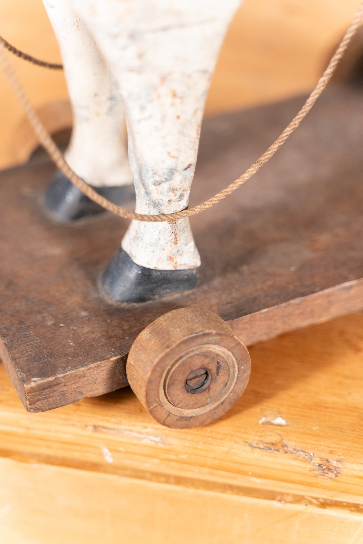 Close-up of a small decorative object with a white animal leg, dark metal feet, a wooden base, and a round wooden wheel on a light wood surface.