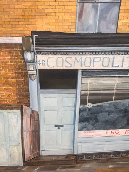 A painted street scene showing a storefront with the sign '46 COSMOPOLIS' above a pale blue door and window display, set against a brick wall.