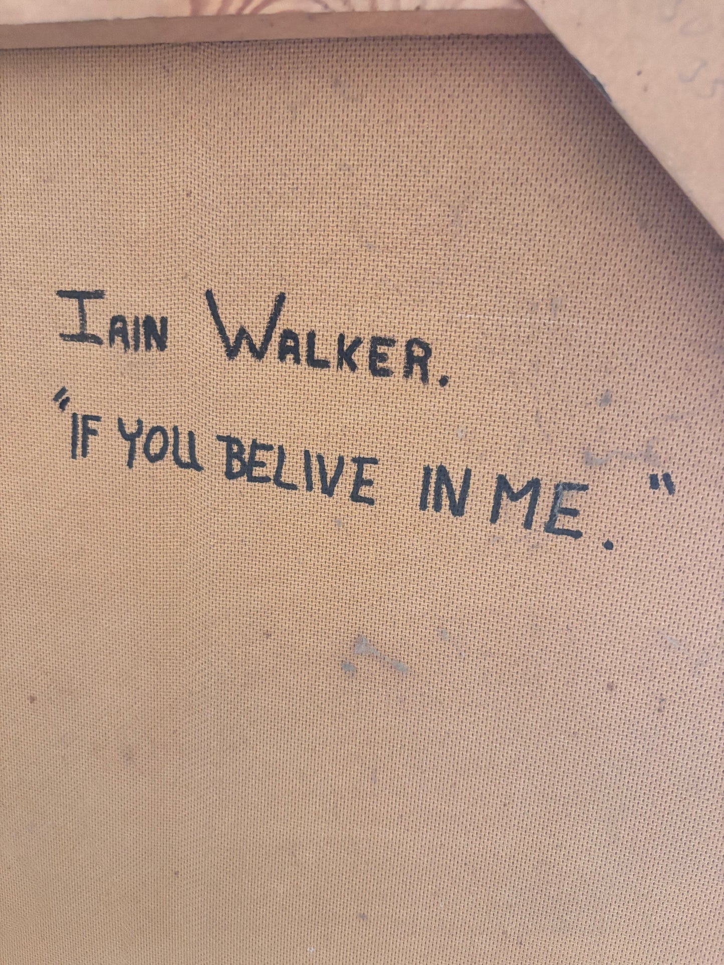 Close-up of a canvas or fabric artwork surface with handwritten text reading 'Iain Walker.' and the quote '"If you believe in me.