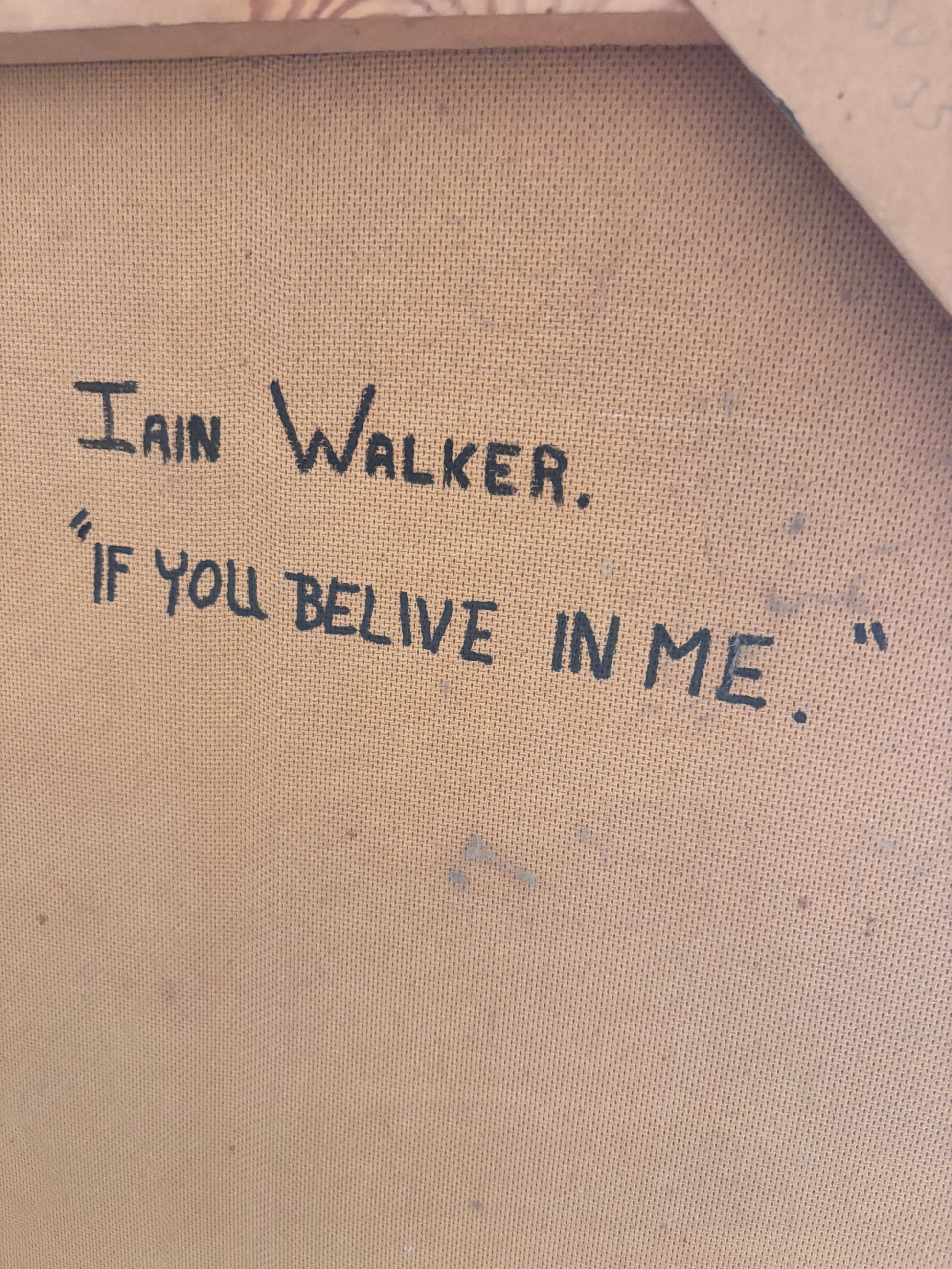 Close-up of a canvas or fabric artwork surface with handwritten text reading 'Iain Walker.' and the quote '"If you believe in me.