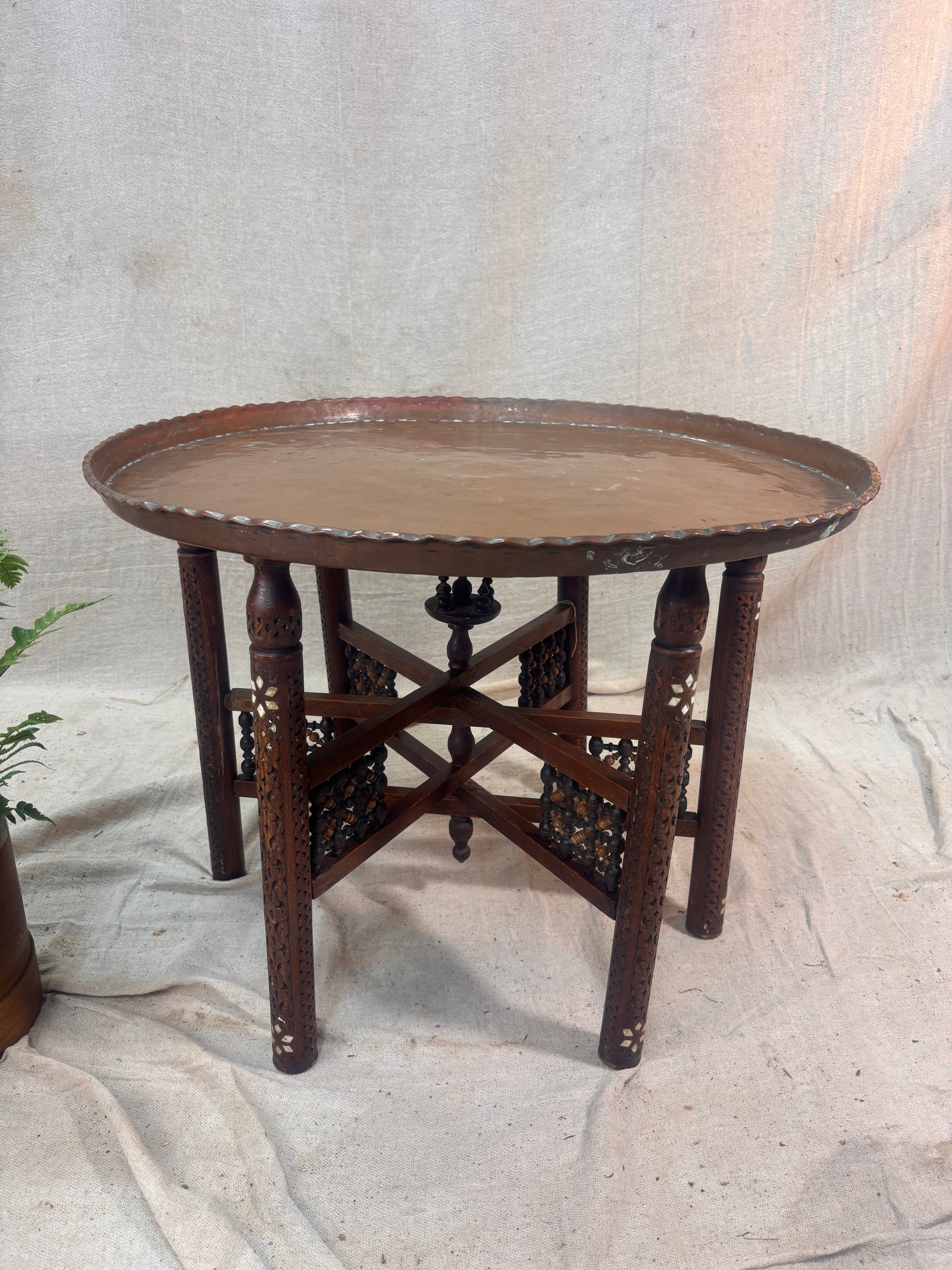 Round metal topped tray table with intricate carved wooden legs on a textured white background