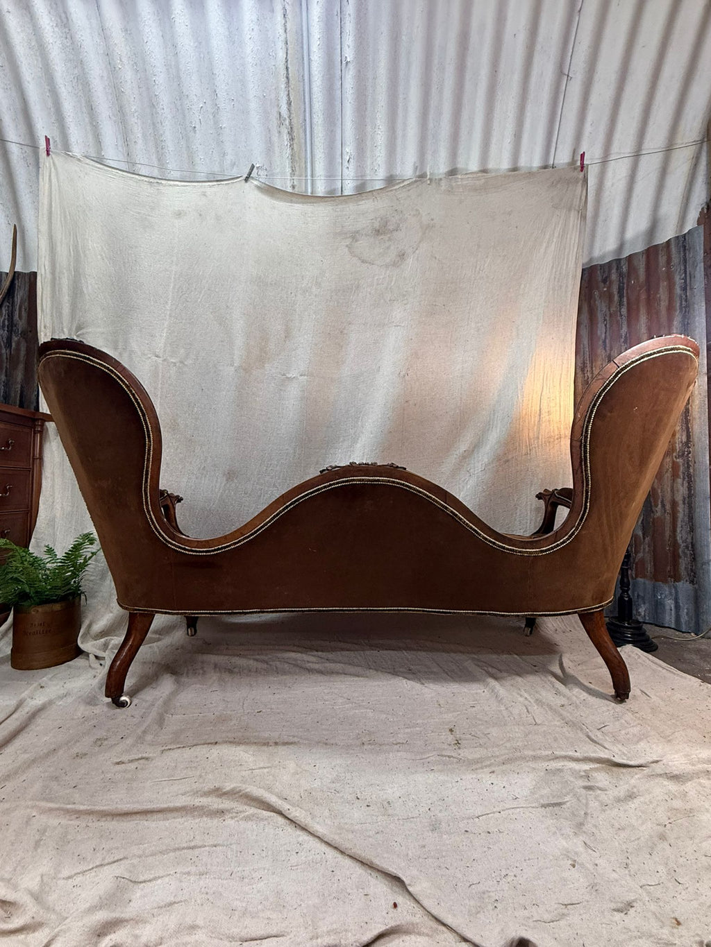 back view of a Vintage brown velvet sofa against a corrugated metal wall.