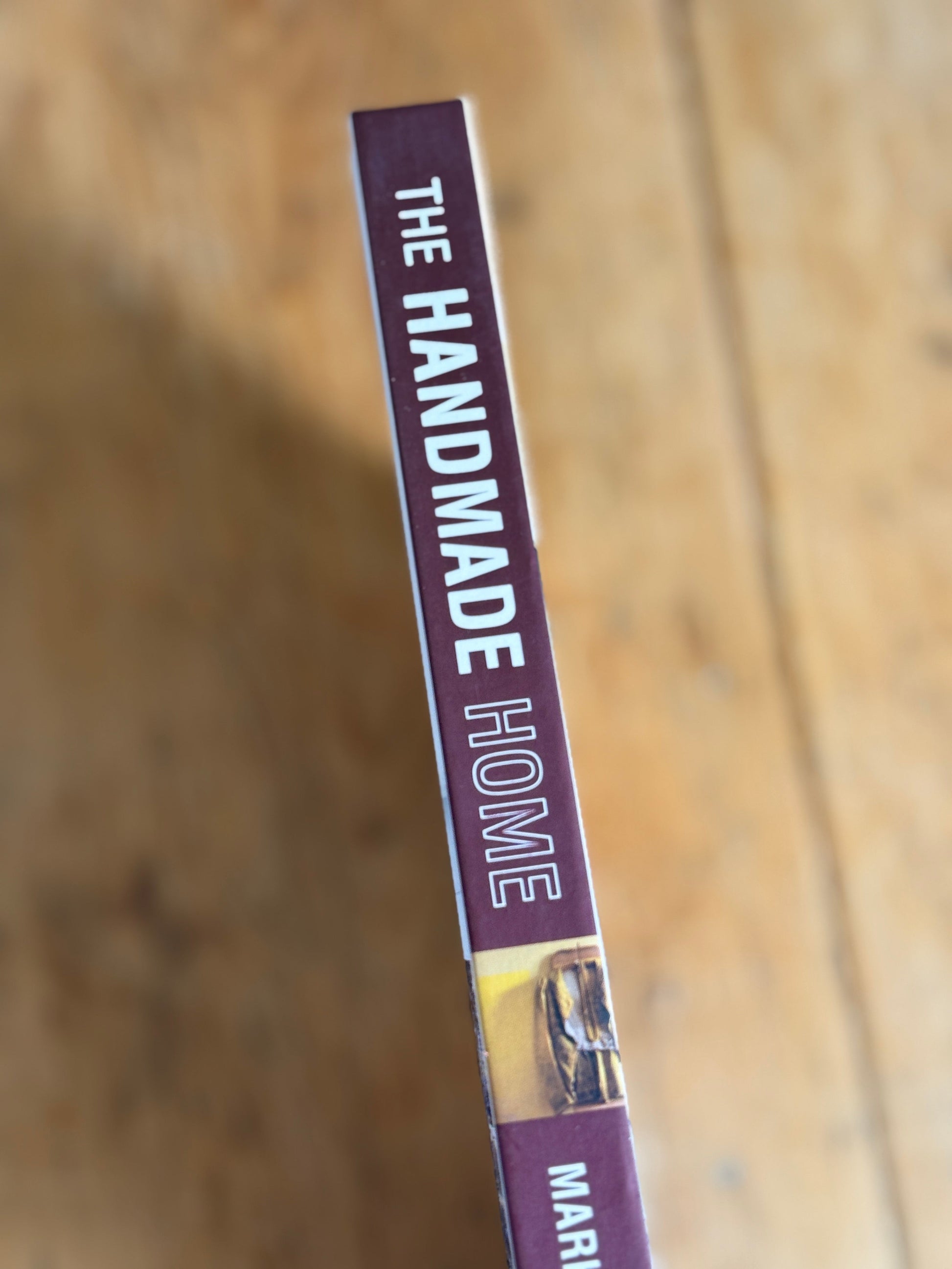 A close-up of a book or magazine cover titled 'THE HANDMADE HOME' on a wooden surface.