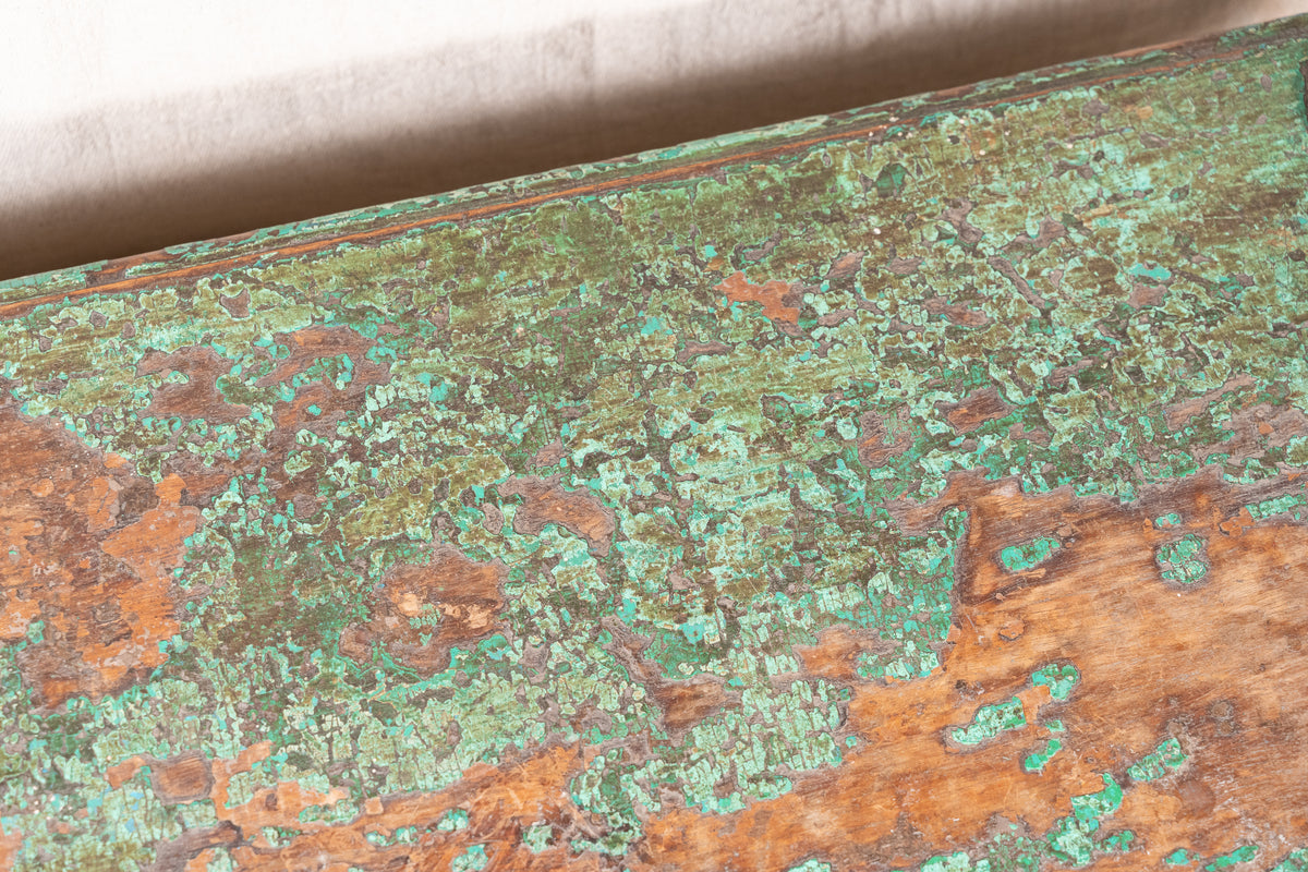 Low wooden bajot table with distressed green paint, angled legs and metal corner rings, possibly repurposed from an old gate or door.