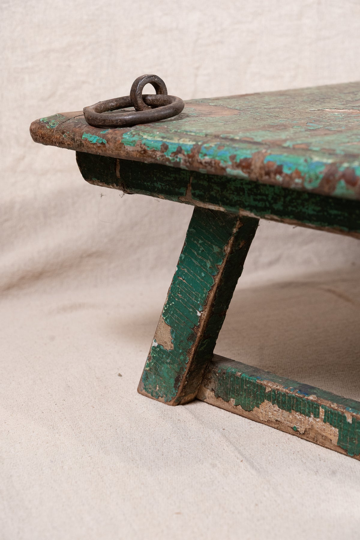 Low wooden bajot table with distressed green paint, angled legs and metal corner rings, possibly repurposed from an old gate or door.