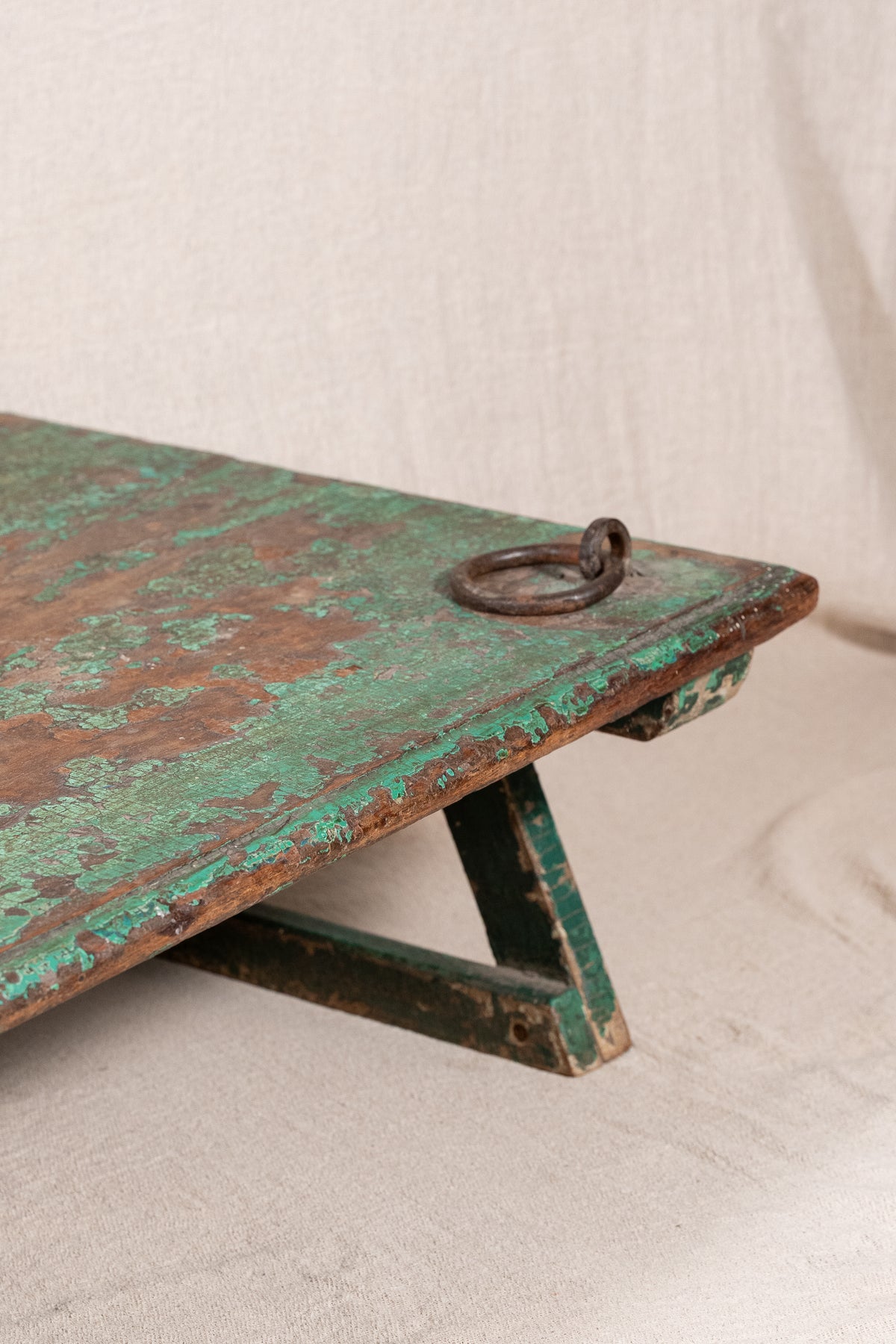 Low wooden bajot table with distressed green paint, angled legs and metal corner rings, possibly repurposed from an old gate or door.