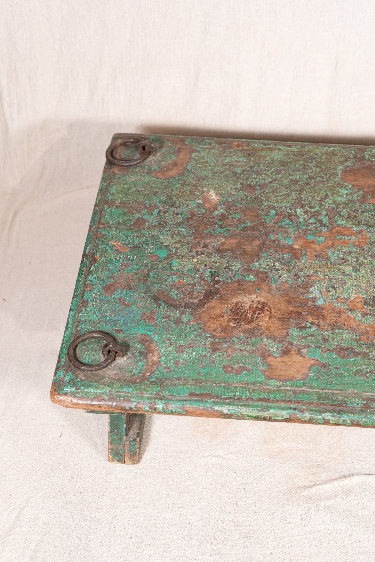 Low wooden bajot table with distressed green paint, angled legs and metal corner rings, possibly repurposed from an old gate or door.