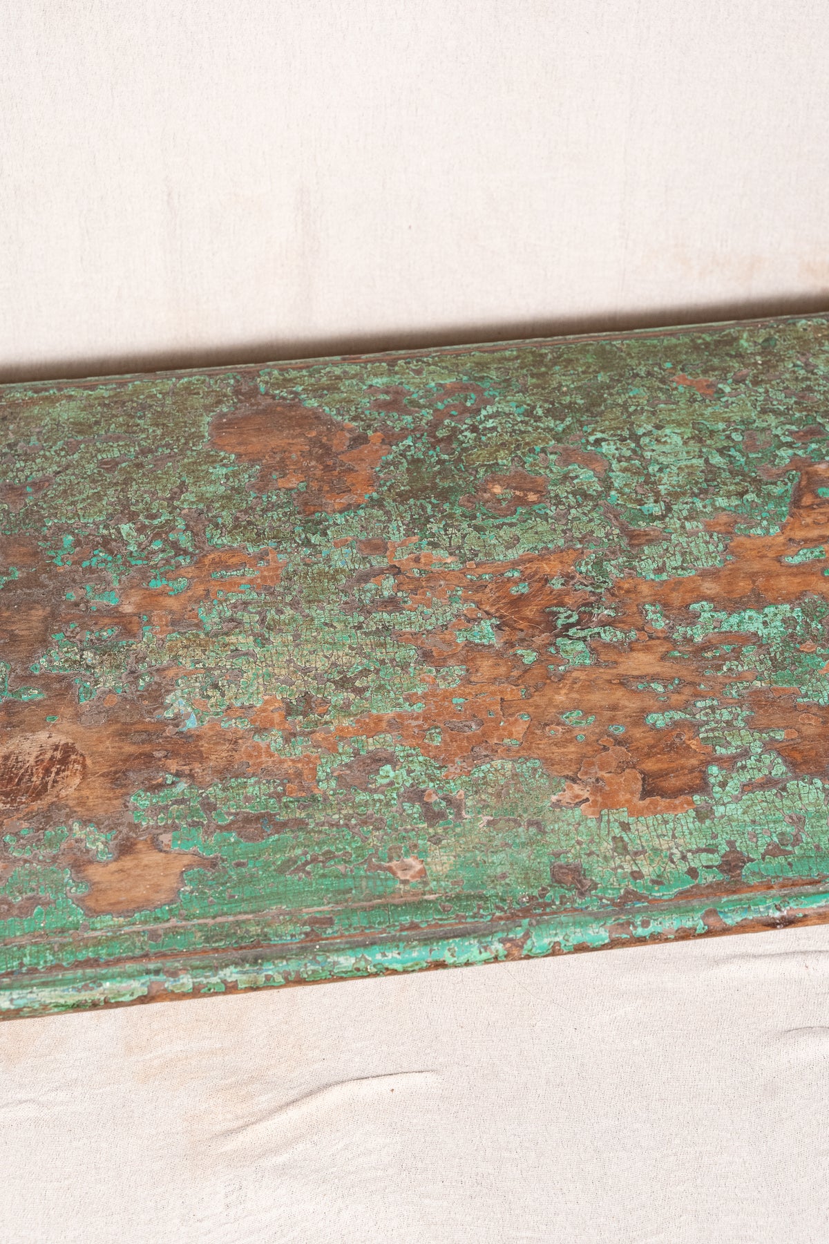 Low wooden bajot table with distressed green paint, angled legs and metal corner rings, possibly repurposed from an old gate or door.