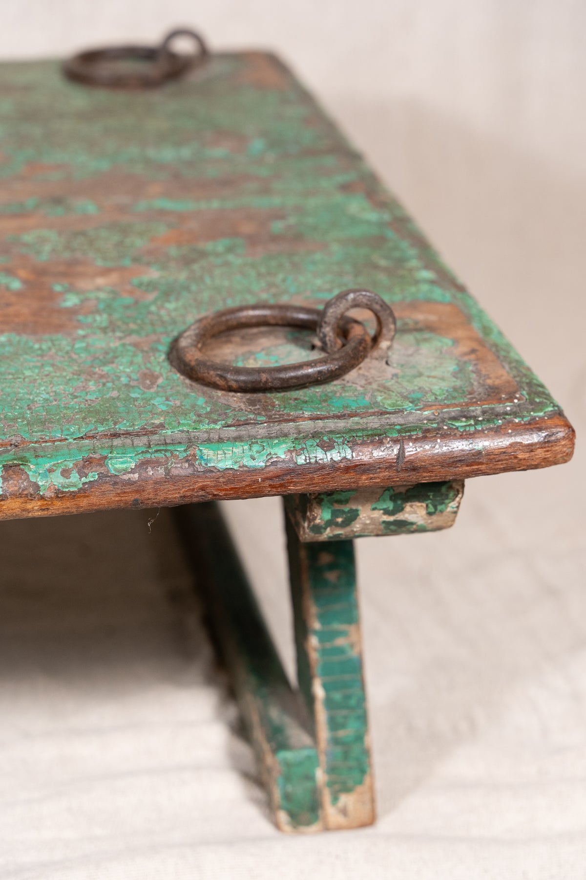 Low wooden bajot table with distressed green paint, angled legs and metal corner rings, possibly repurposed from an old gate or door.