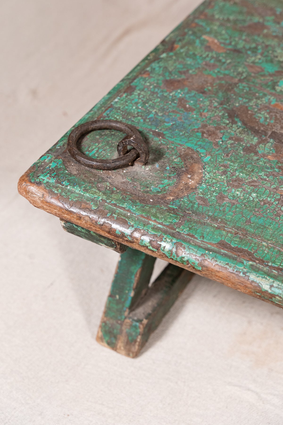 Low wooden bajot table with distressed green paint, angled legs and metal corner rings, possibly repurposed from an old gate or door.